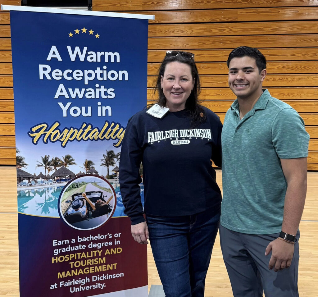 Two people stand next to a banner promoting the hospitality program.