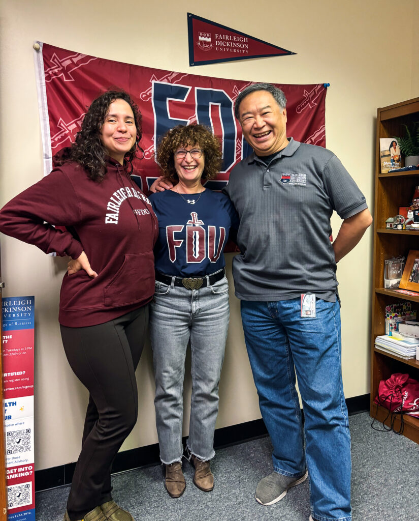 Three people wearing FDU-branded clothes smile for a photo.