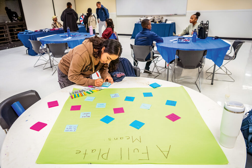 A student writes on a sticky note to add to poster board.