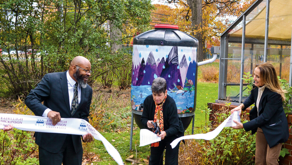Three people cut a ribbon to celebrate a rain barrel on campus.
