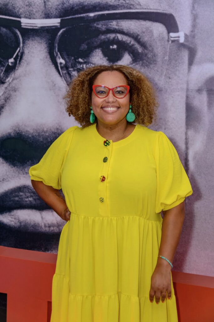 Terza Lima-Neves smiles at the camera. she wears a yellow dress.