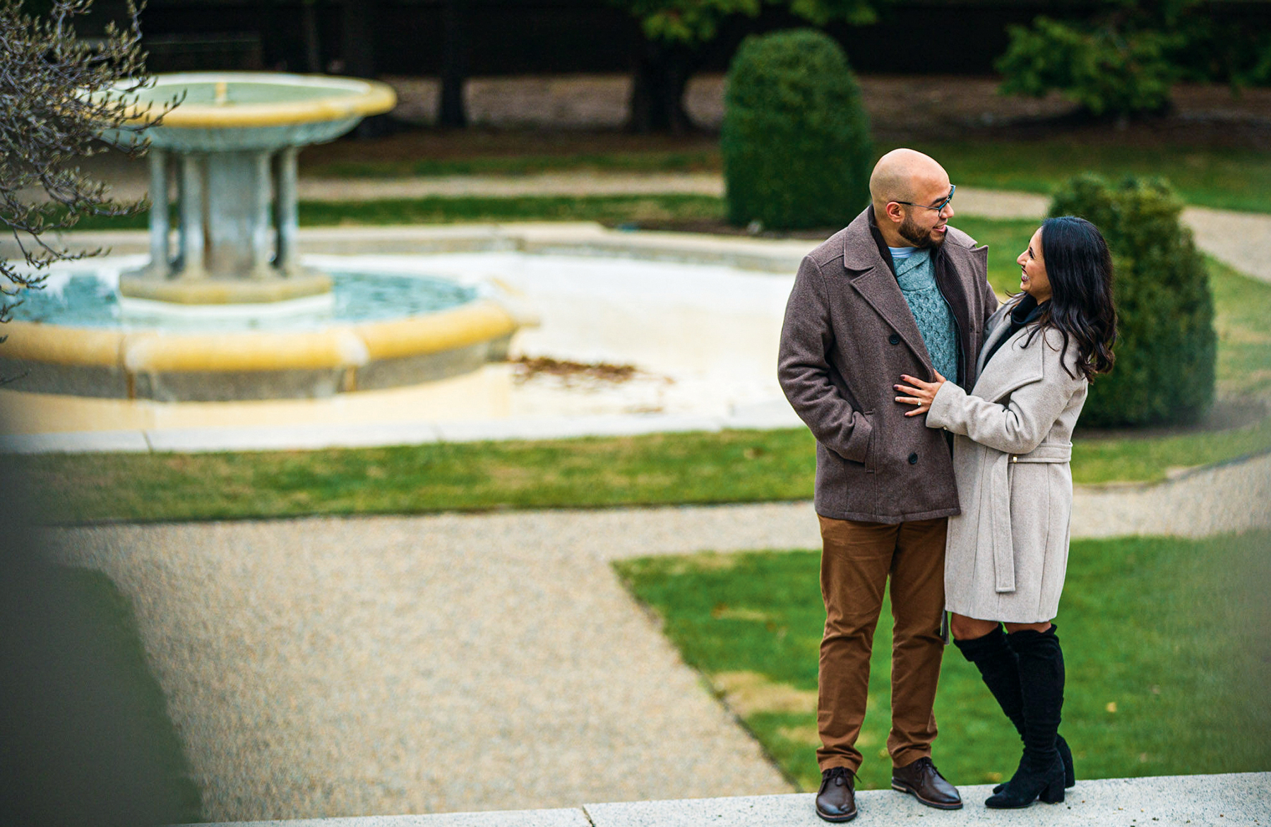 A couple share an embrace outside near a fountain.