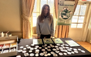 a woman stands at a table and smile for the photo. on the tables are signs and stickers.