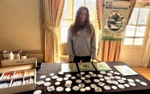 a woman stands at a table and smile for the photo. on the tables are signs and stickers.