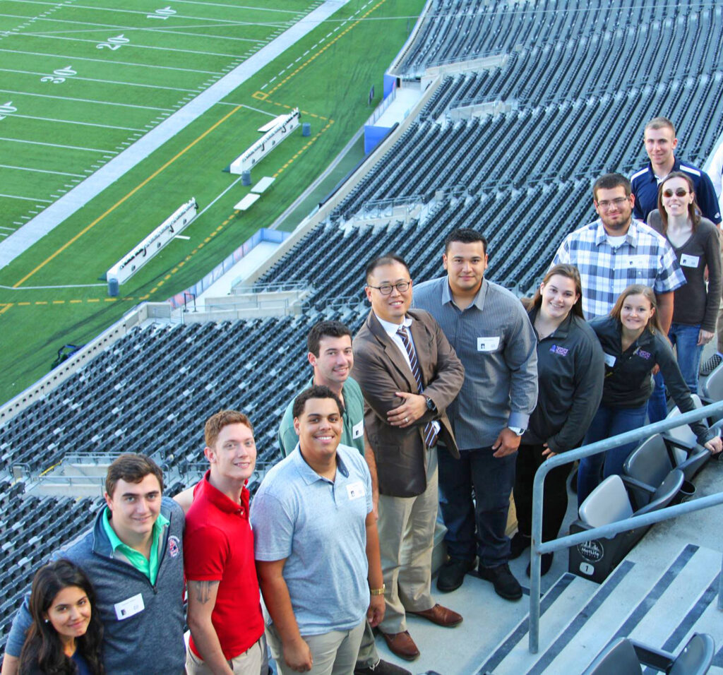 Students faculty stand in the bleachers at a major football stadium.
