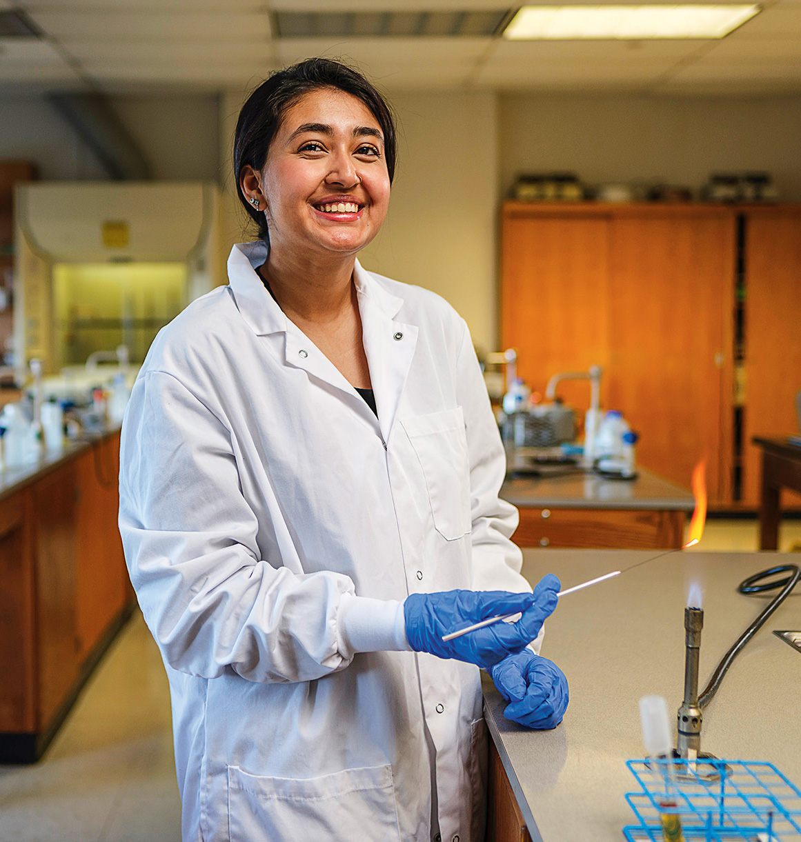 A young woman wearing a white lab coat conducts an experiment in a science lab.