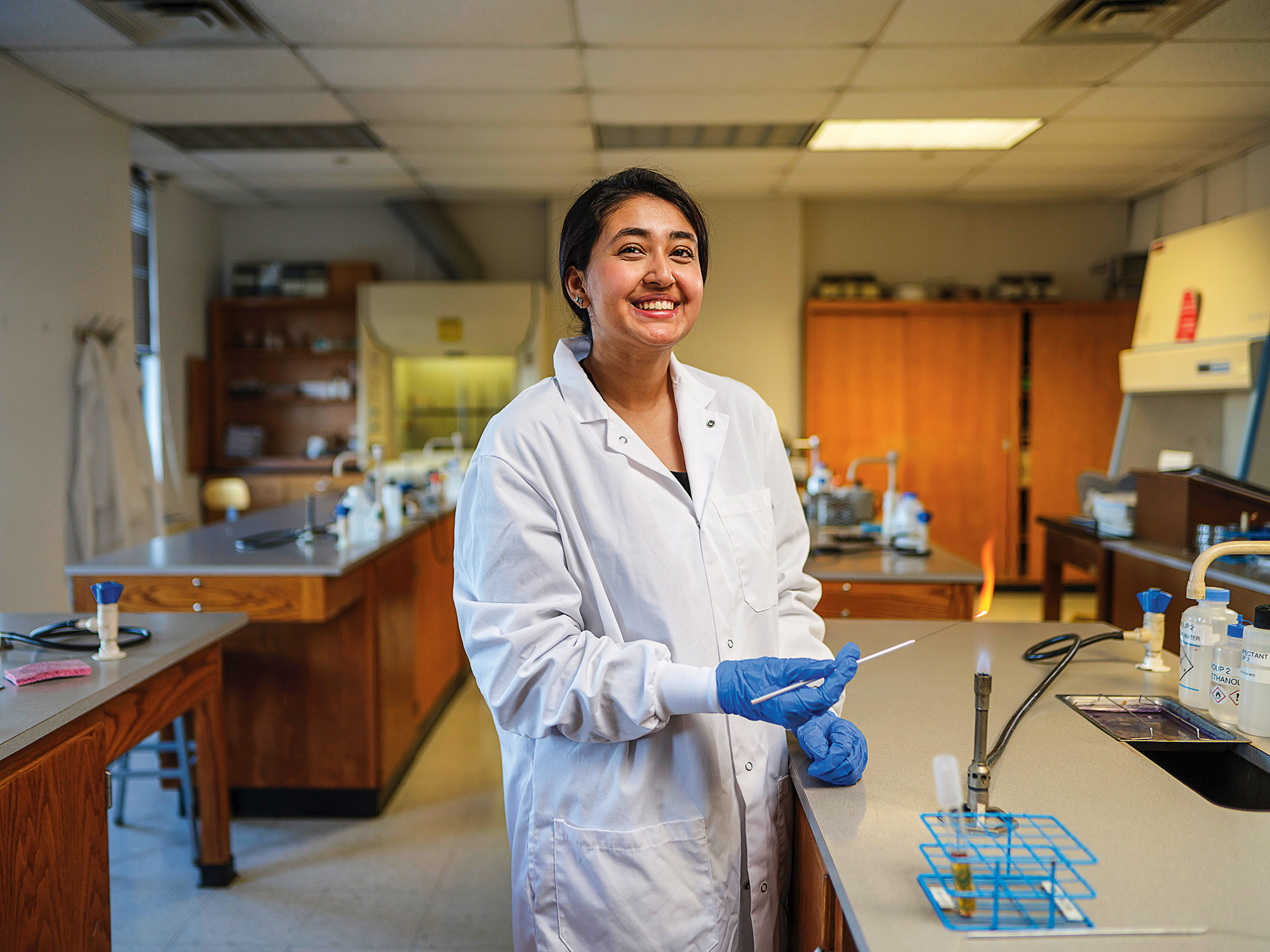 A young woman wearing a white lab coat conducts an experiment in a science lab.