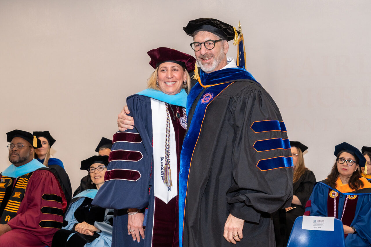 a doctorate student and a professor wear regalia and smile.