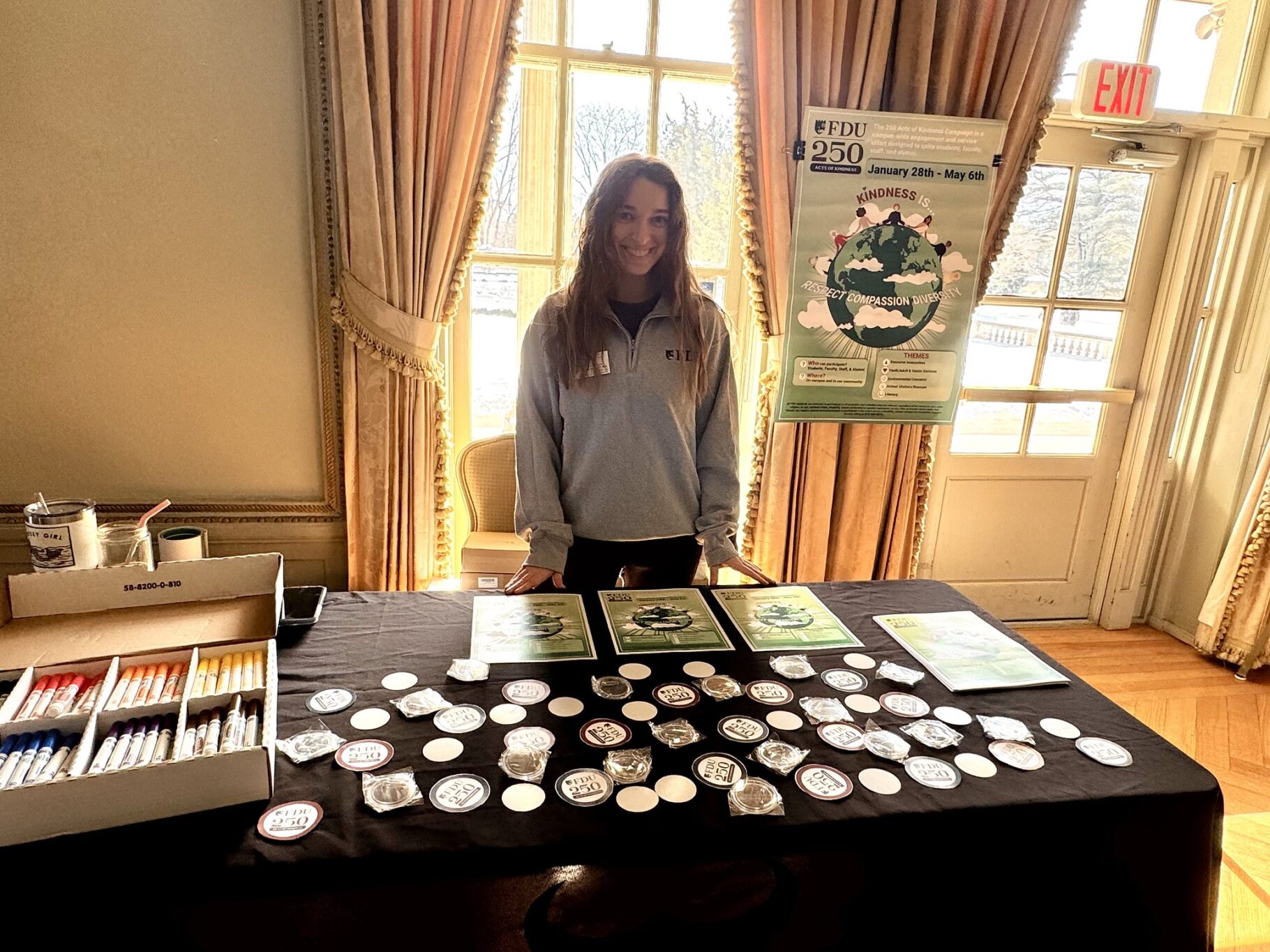 a woman stands at a table and smile for the photo. on the tables are signs and stickers.