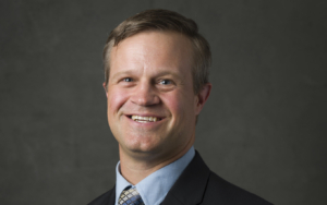 a headshot of a man. he wears a suit.