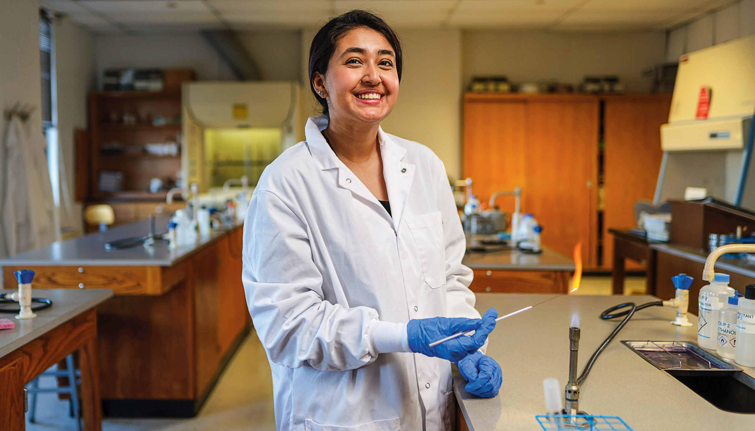 A young woman wearing a white lab coat conducts an experiment in a science lab.