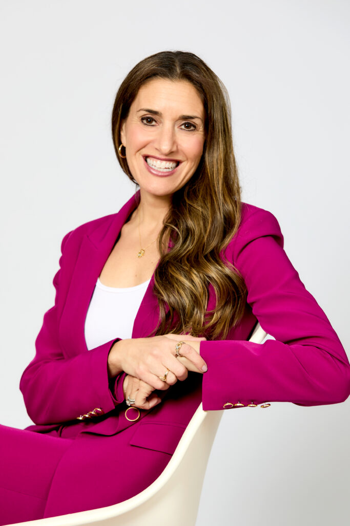 a headshot of a woman. she wears a pink blazer and matching pants.