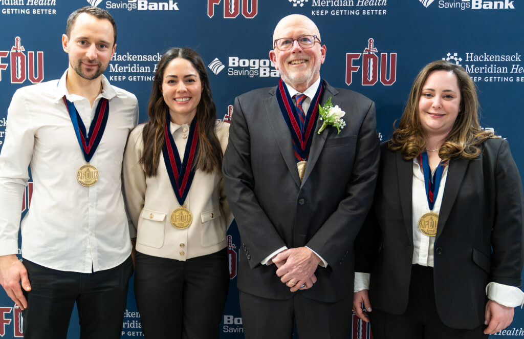 Four people standing in a row smiling and wearing medals