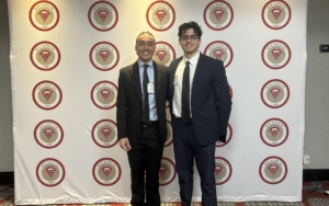 two men stand in front of a backdrop.
