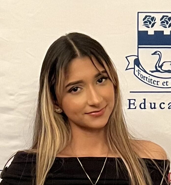 Student at an FDU Educational Opportunity Fund event holds three program folders while standing in front of a university banner featuring the school's swan crest logo.