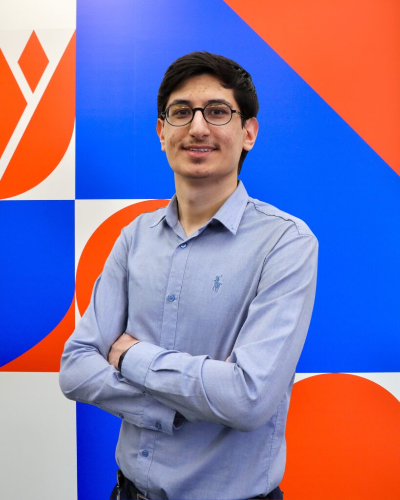 A young man wearing glasses poses for a photo with his arms folded.