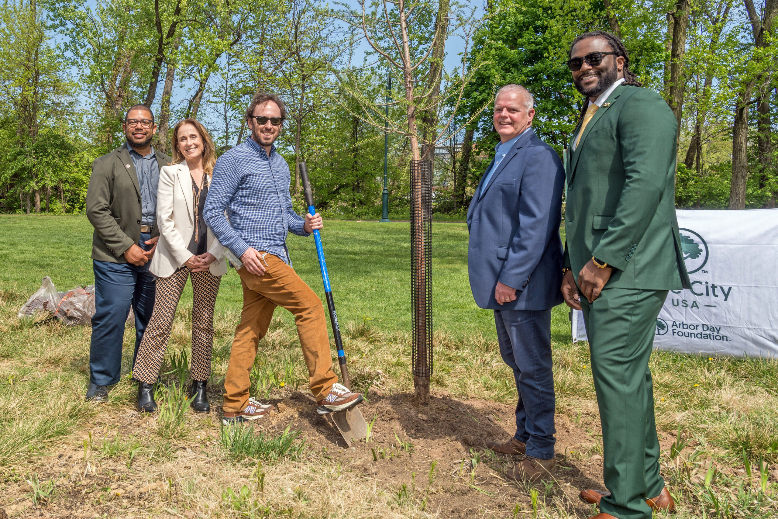 Five people stand around a freshly planted tree.