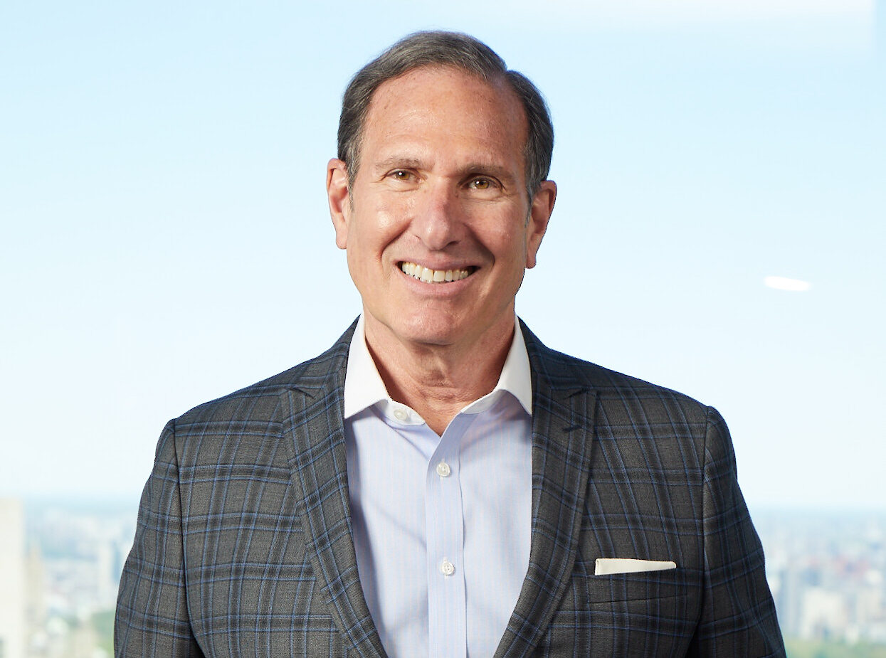 Headshot of Al Lustgarten, a smiling man with short brown hair wearing a gray plaid blazer over a light blue button-down shirt