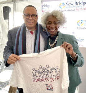 A man and woman smiling and holding up a t-shirt that says Kindness is Free