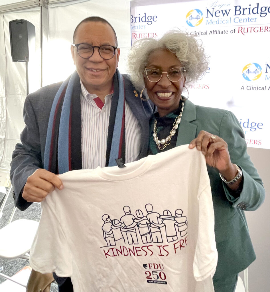 A man and woman smiling and holding up a t-shirt that says Kindness is Free