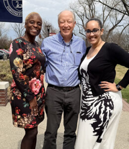 Two women and a man are smiling outside a school building.