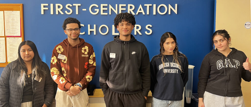 Group of five smiling students in front of a wall that reads Center for First Generation Scholars