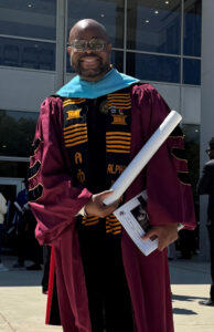 A man wearing academic regalia outside a building.