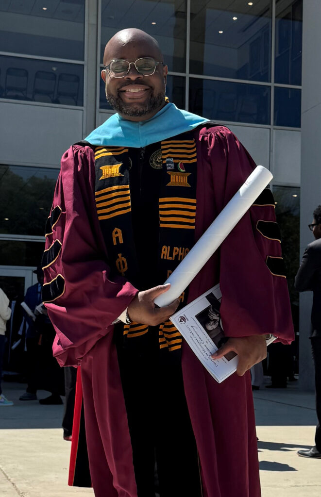 A man wearing academic regalia outside a building.