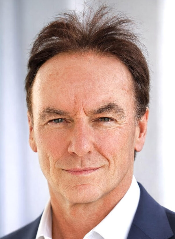 Headshot of John McKenna, a man with short brown hair wearing a dark suit jacket and a light blue collared shirt.