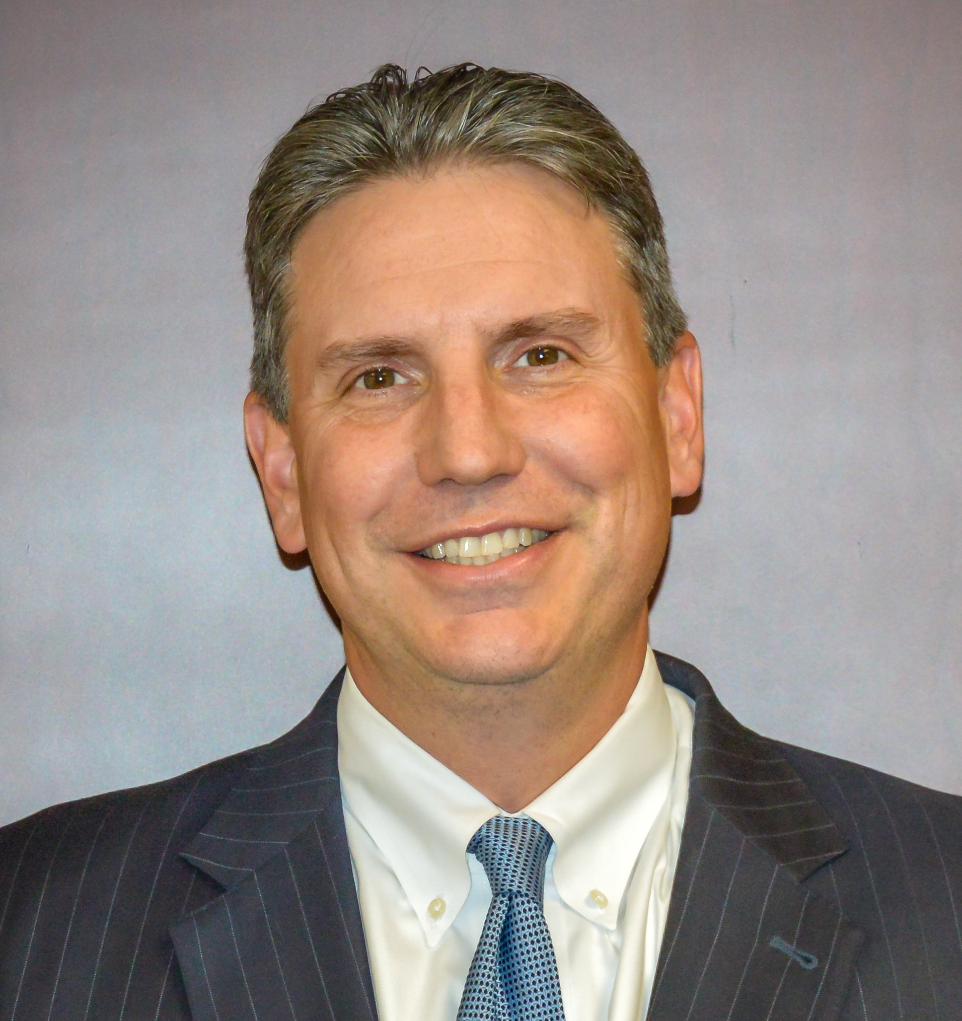 A headshot of Kevin D. Mahn, a smiling man with short graying hair, wearing a dark suit, white shirt, and a light blue tie.