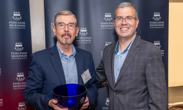 Two men in suits smiling with the one on the left holding an FDU bowl