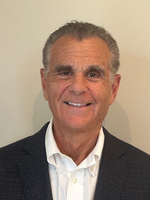 A headshot of Patrick A. Cozza, a smiling man with short gray hair, wearing a dark suit jacket over a white open-collar shirt.