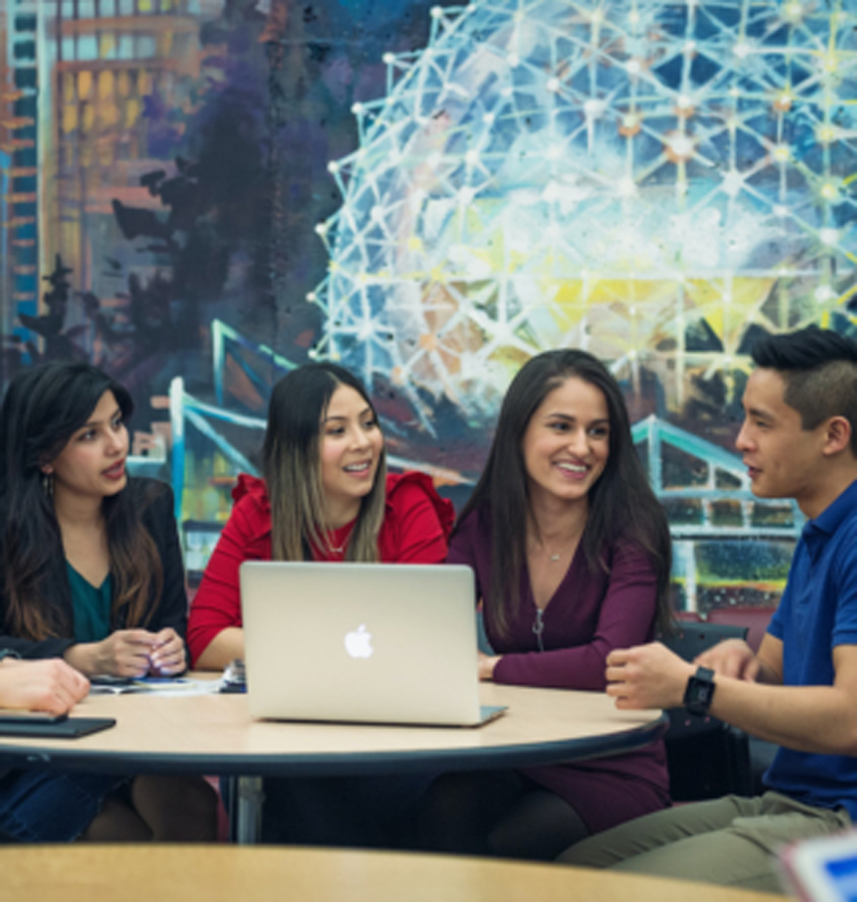 students sits around a laptop and talk to each other.