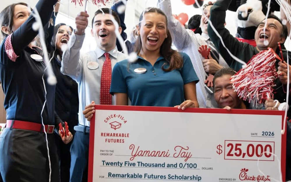 Celebrations surround a young woman as she holds up a large check for $25,000.