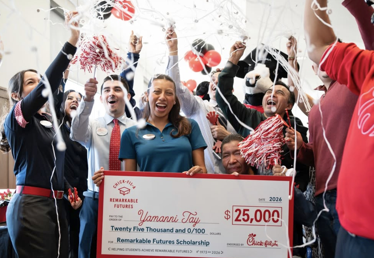 Celebrations surround a young woman as she holds up a large check for $25,000.