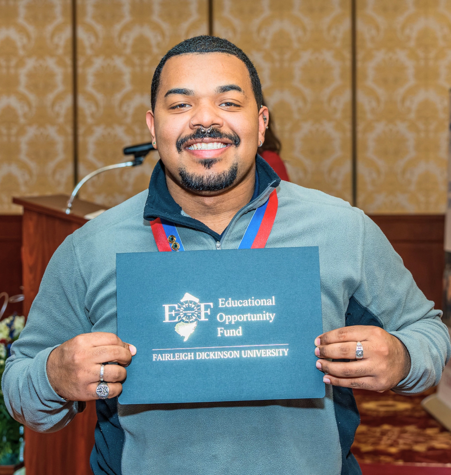 a student holds up a certificate and smiles at the camera. the certificate folder reads 