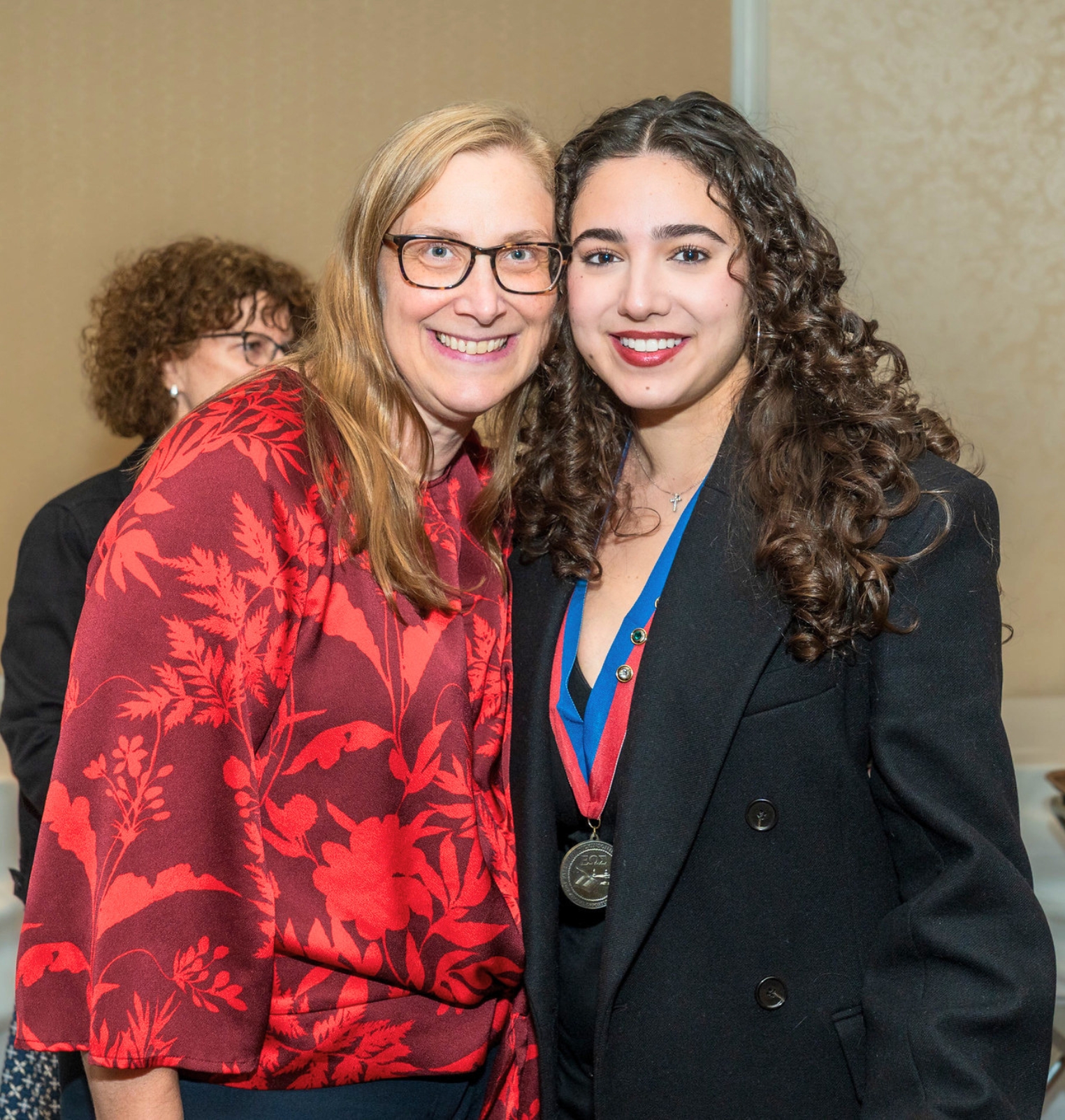 a college student and a staff member smile for the camera. the student wears a medal.