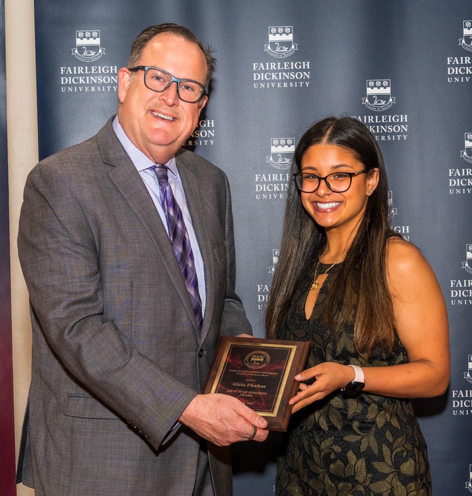 a college student accepts an award from a college staff member. the award is a plaque.