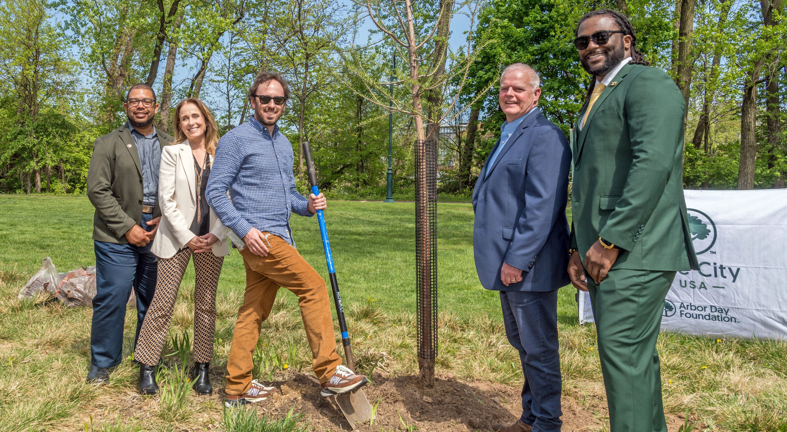 Five people stand around a freshly planted tree.