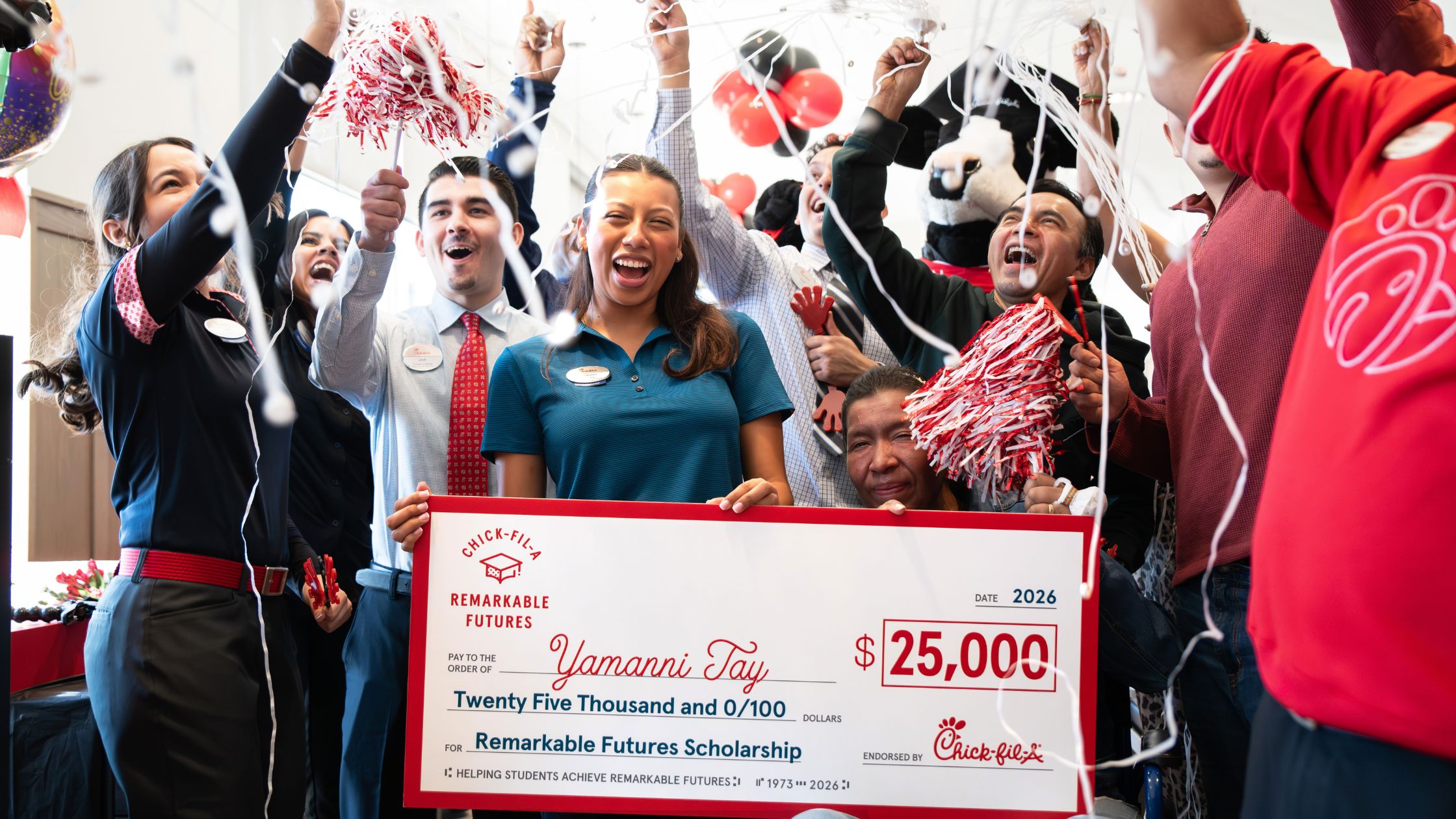 Celebrations surround a young woman as she holds up a large check for $25,000.