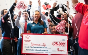 Celebrations surround a young woman as she holds up a large check for $25,000.