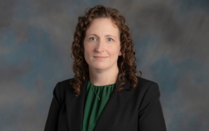 Woman poses against a backdrop. she wears a blazer.