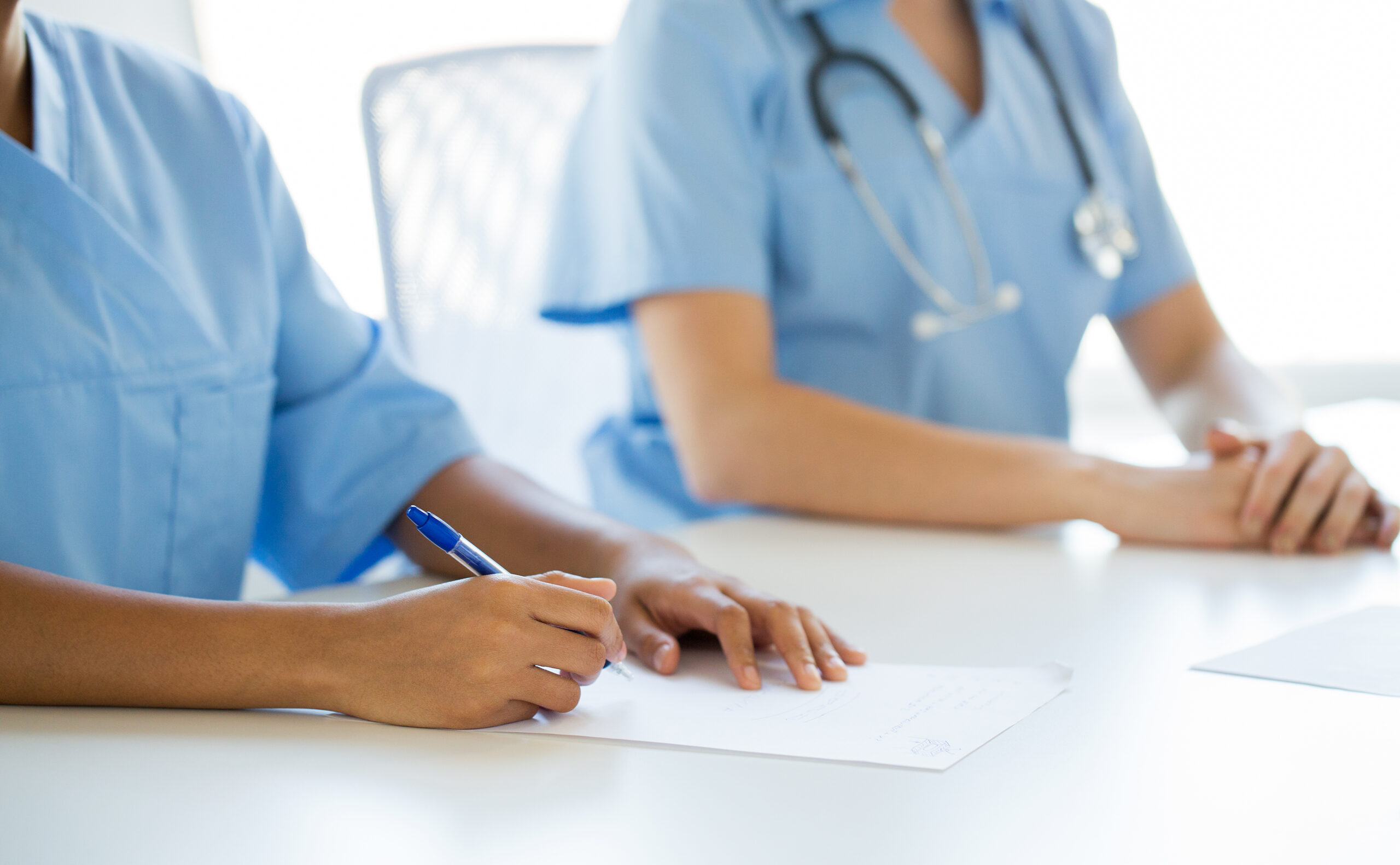 Two healthcare workers in scrubs sit side by side, shown from the neck down.