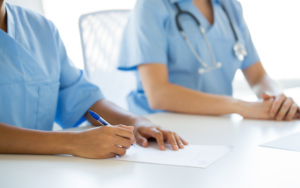 Two healthcare workers in scrubs sit side by side, shown from the neck down.