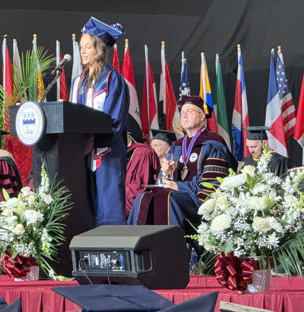 A young woman in a cap and gown speaks to the crowd at graduation.