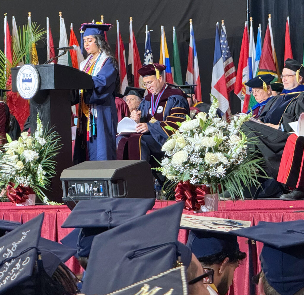A young woman in a cap and gown speaks to the crowd at graduation.