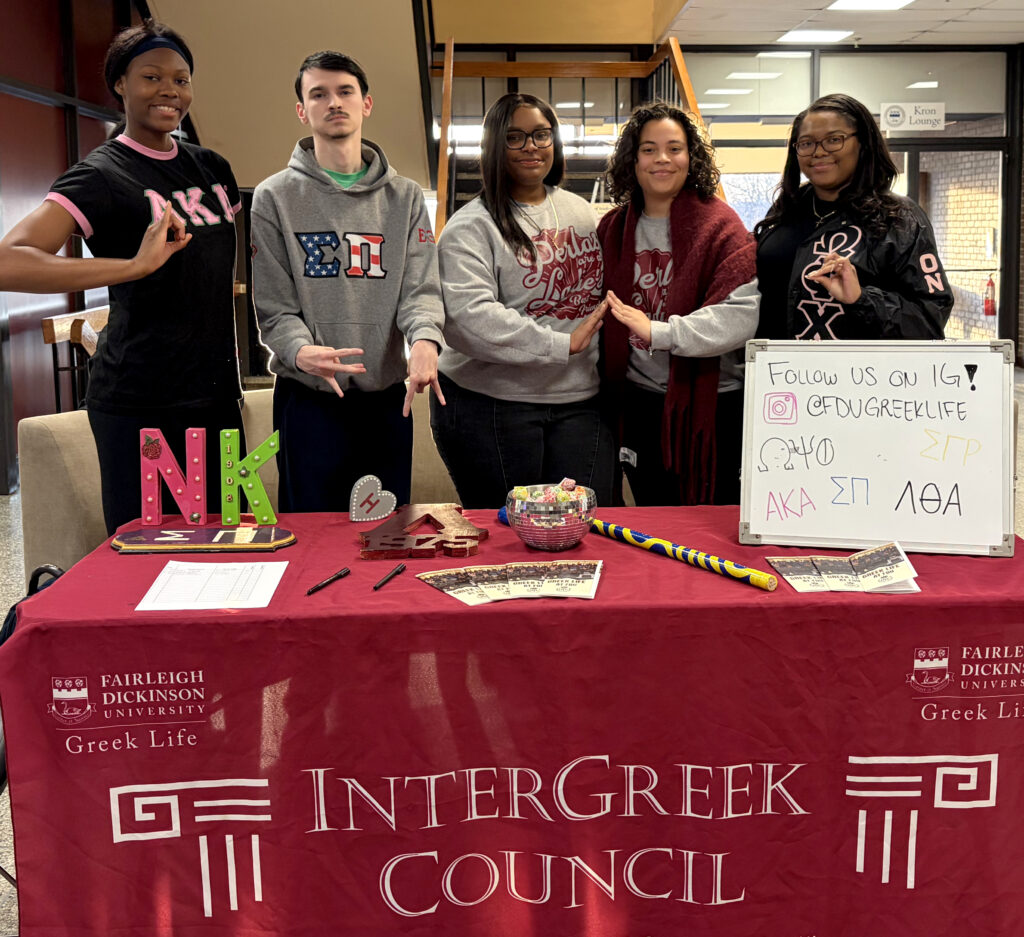 A group of smiling male and female students in front of a desk.