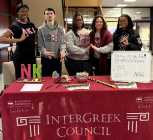 A group of smiling male and female students in front of a desk.