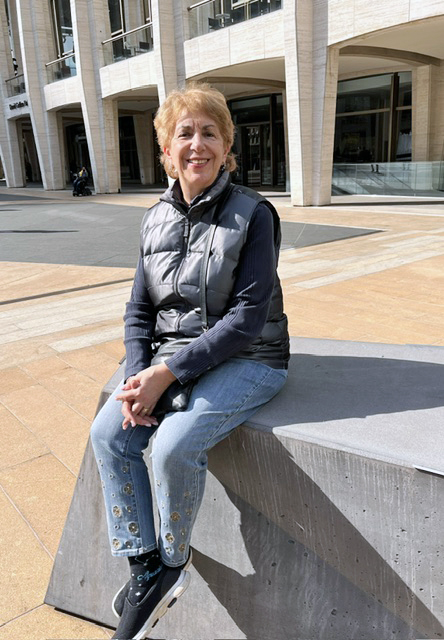 A woman sits perched on a retaining wall outside.