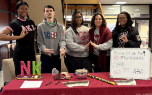 A group of smiling male and female students in front of a desk.